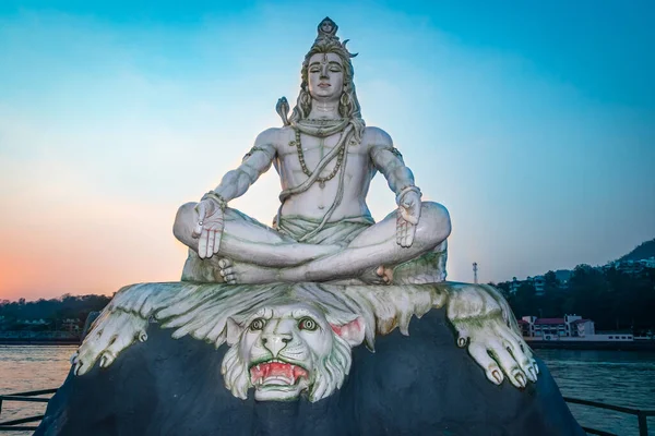 hindu god lord shiva statue in meditation posture with dramatic sky at evening from unique angle image is taken at parmarth niketan rishikesh uttrakhand india.