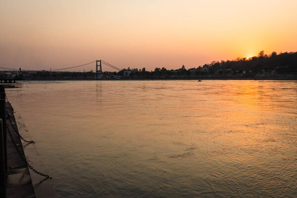 sunset orange sky over flowing river horizon at evening from flat angle image is taken at rishikesh uttrakhand india.