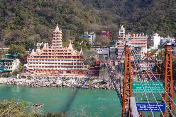 Gangsterler nehir kıyısındaki eski Hindu tapınağı. 15 Mar 2022 'de Hindistan' daki Lakshman jhula rishikesh uttrakhand tapınağında gün içinde düz açılı görüntüden demir köprü başı çizgisi çekiliyor..