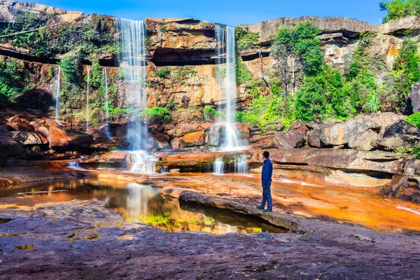 Yansıması ve mavi gökyüzü ile dağdan düşen şelaleyi izleyen izole genç adam.