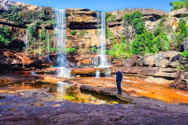 Yansıması ve mavi gökyüzü ile dağdan düşen şelalenin yanında duran izole genç adam.