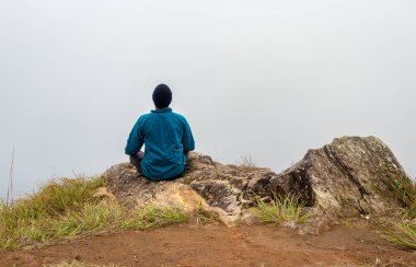 Düz açılı beyaz sisli bir adam dağ kayasında meditasyon yapıyor.