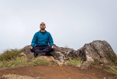 Düz açılı beyaz sisli bir adam dağ kayasında meditasyon yapıyor.