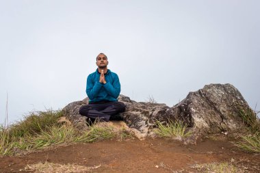 Düz açılı beyaz sisli bir adam dağ kayasında meditasyon yapıyor.
