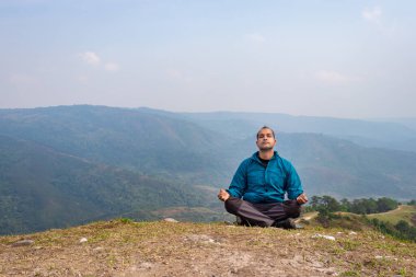 Tepenin zirvesinde sisli dağ öfkesiyle meditasyon yapan bir adam düz açılı görüntüden Hindistan 'da çekilmiştir..
