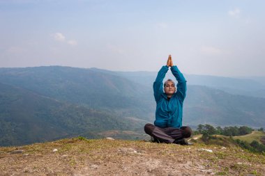 Tepenin zirvesinde sisli dağ öfkesiyle meditasyon yapan bir adam düz açılı görüntüden Hindistan 'da çekilmiştir..