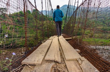 man sitting alone at vintage iron suspension bridge from low angle image is taken at nongjrong meghalaya india.