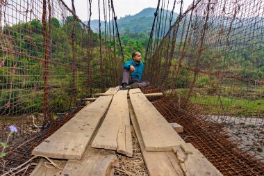 man sitting alone at vintage iron suspension bridge from low angle image is taken at nongjrong meghalaya india.