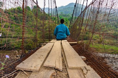 man meditating at vintage iron suspension bridge from low angle image is taken at nongjrong meghalaya india.