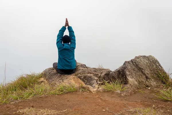 Düz açılı beyaz sisli bir adam dağ kayasında meditasyon yapıyor.
