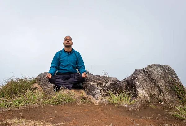 Düz açılı beyaz sisli bir adam dağ kayasında meditasyon yapıyor.