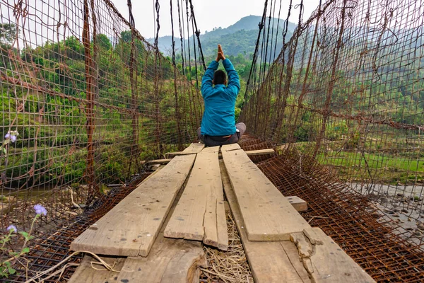 man meditating at vintage iron suspension bridge from low angle image is taken at nongjrong meghalaya india.