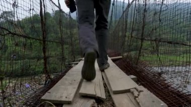Delikanlı, sabahın köründe eski demir askı köprüsünde düz açıyla yürüyor.