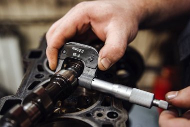 Eldeki bir ölçüm cihazı, bir arabanın arka planına karşı, derin bir alan derinliğindeki kam milini ölçer.