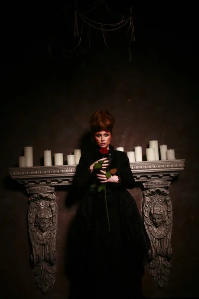 Gothic girl standing near candles with red rose — Stock Photo, Image