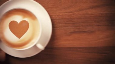 Kahveyi kalp sembolü latte sanatıyla servis eden bir elin üst görüntüsü.