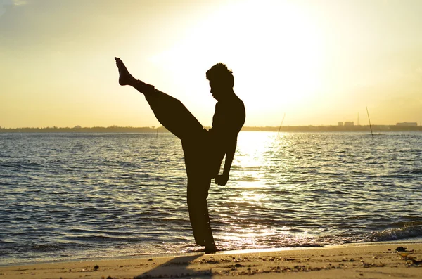 Silhouette of young boy performing a pencak silat, Malay traditional discipline martial art in evening at the beach — Stock Photo, Image