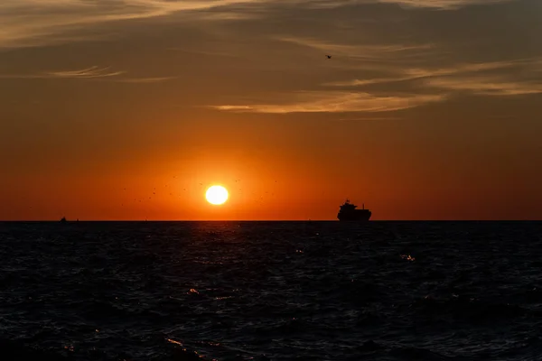 Sylwetka statku na horyzoncie, idącego w stronę zachodzącego słońca. — Zdjęcie stockowe