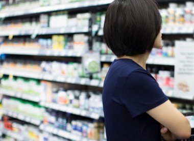 Market Eczanesinden Kadın Alışverişi. Süpermarkette alışveriş yapan biri. Kadın Tutucu Sepeti, hangi ürünü alacağına karar vermeye çalışıyor. Perakende Sağlık Sigortası, Vitamin ve İlaveleri.