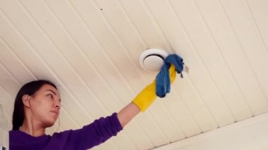 Tavan lambasına temizleyici bez ile toz temizleyen bir kadın.