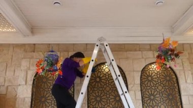 Genç Asyalı kız merdivenin üstünde duruyor tavanı ve sarı eldivenleri siliyor.