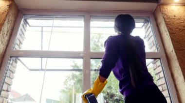 Düşük açılı Asyalı kadın pencereye su serper ve yıkayıp siler.