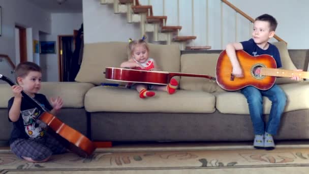 Маленькая девочка и два мальчика играют на классической гитаре, сидя на диване. Стоковое Видео