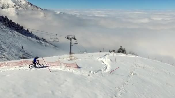 Vista aérea acima de um homem de bicicleta de montanha na neve, tiro drone. acima das nuvens — Vídeo de Stock