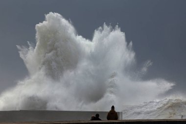 Deniz rıhtımında fırtına dalgalar, büyük bir sıçrama ve izleyen insanlar..