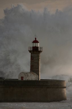 Eski deniz fenerinde büyük bir fırtına dalgası ve Portekiz 'in kuzeyindeki Douro nehrinin ağzından granit iskele. Bulutlu gün batımı.