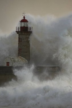 Eski deniz fenerinde büyük bir fırtına dalgası ve Portekiz 'in kuzeyindeki Douro nehrinin ağzından granit iskele. Bulutlu gün batımı.