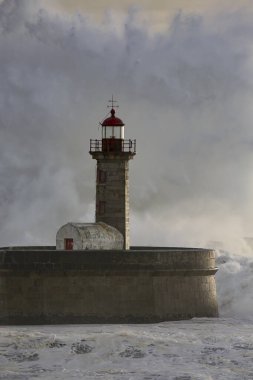 Eski deniz fenerinde büyük bir fırtına dalgası ve Portekiz 'in kuzeyindeki Douro nehrinin ağzından granit iskele. Bulutlu gün batımı.