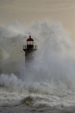 Eski deniz fenerinde büyük bir fırtına dalgası ve Portekiz 'in kuzeyindeki Douro nehrinin ağzından granit iskele. Bulutlu gün batımı.