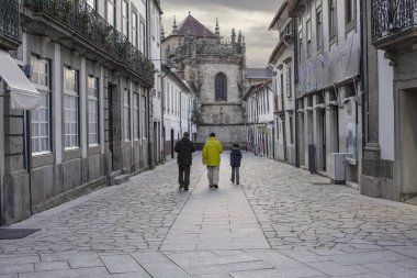 Braga, Portekiz - 1 Nisan 2010: Eski sokak önlerinde ortaçağ kilisesi ve oradan geçen insanlar. Günün sonunda gün ışığı.