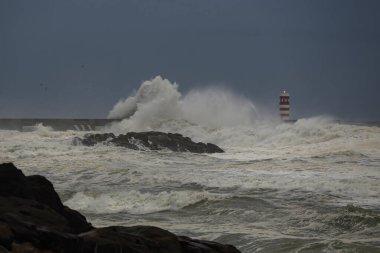 Alacakaranlıkta deniz fırtınası. Douro nehri ağzı kuzey rıhtımı ve alacakaranlıkta fener..