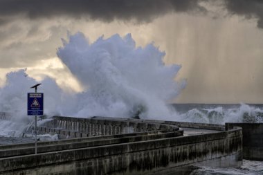 Yumuşak arkadan aydınlatmalı büyük dalga sıçrama. Fırtınalı gün batımı ışık yağmur görmek. Douro nehir ağzı Güney iskele ve işaret. (Uyarı işareti diyor ki: dikkat, tehlike, deniz bölgesi overtopping)
