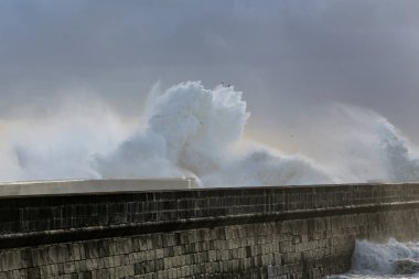 Fırtınalı dalgalar günbatımında veya alacakaranlıkta sıçrar. Yaşlı Douro nehri ağzı güney duvarı, Porto, Portekiz.