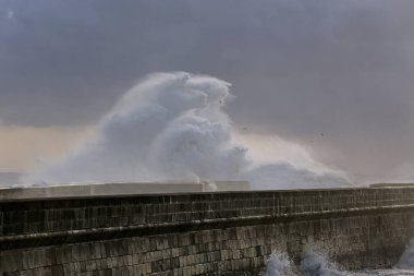 Big wave splash over pier against a dark sky at dusk