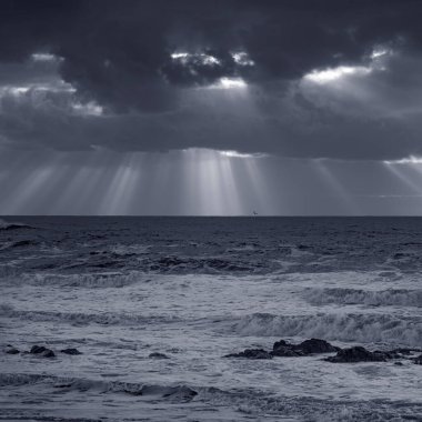 Stormy seascape with dramatic clouds and sunbeams. Used infrared filter.. Toned blue.