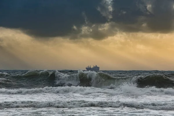 Commercial ship on the horizon in a stormy sunset with sunbeams.