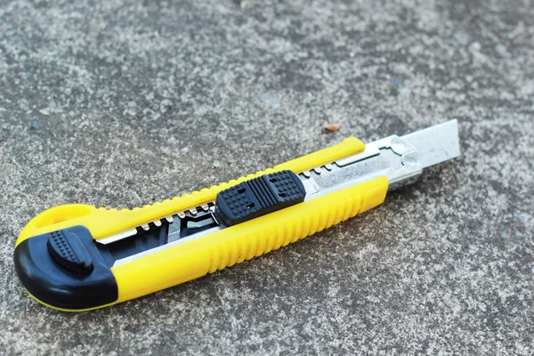 The yellow stationery knife on a cement floor. — Stock Photo, Image