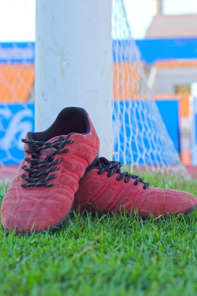 Rode schoenen op groen gras met doel voetbal — Stockfoto