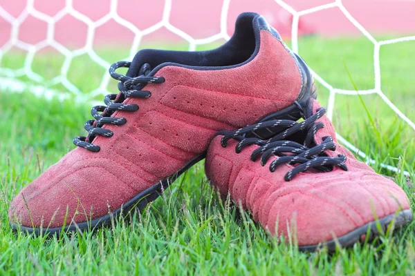 Sapatos vermelhos na grama verde com gol de futebol — Fotografia de Stock