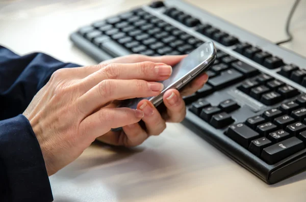 Mobile in hands and keyboard — Stock Photo, Image