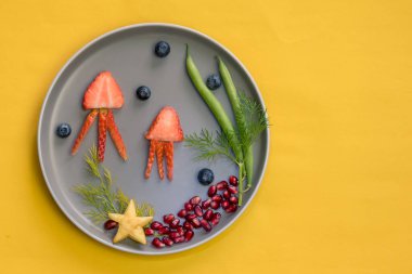 Çilek, böğürtlen, fasulye ve nar gibi sarı arkaplanlı tenha yemek fikirlerinden denizanası, yeşil bitkiler ve deniz yıldızı.