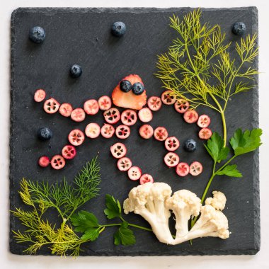 ahtapot deniz dünyası ile kırmızı meyvelerden yapılır karnabahar ve siyah arka planda yeşil otlar