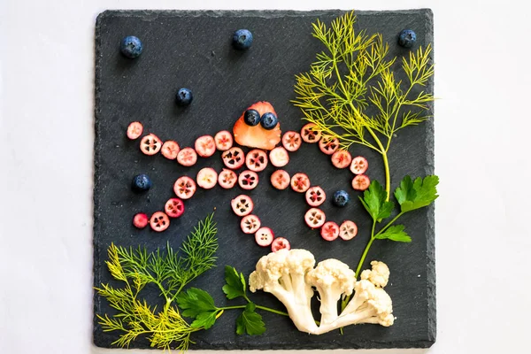 ahtapot deniz dünyası ile kırmızı meyvelerden yapılır karnabahar ve siyah arka planda yeşil otlar