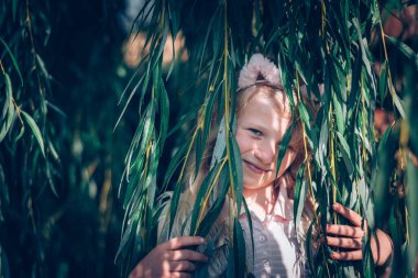 Uzun sarı saçlı tatlı genç kız ilkbaharda söğüt ağacıyla eğleniyor.
