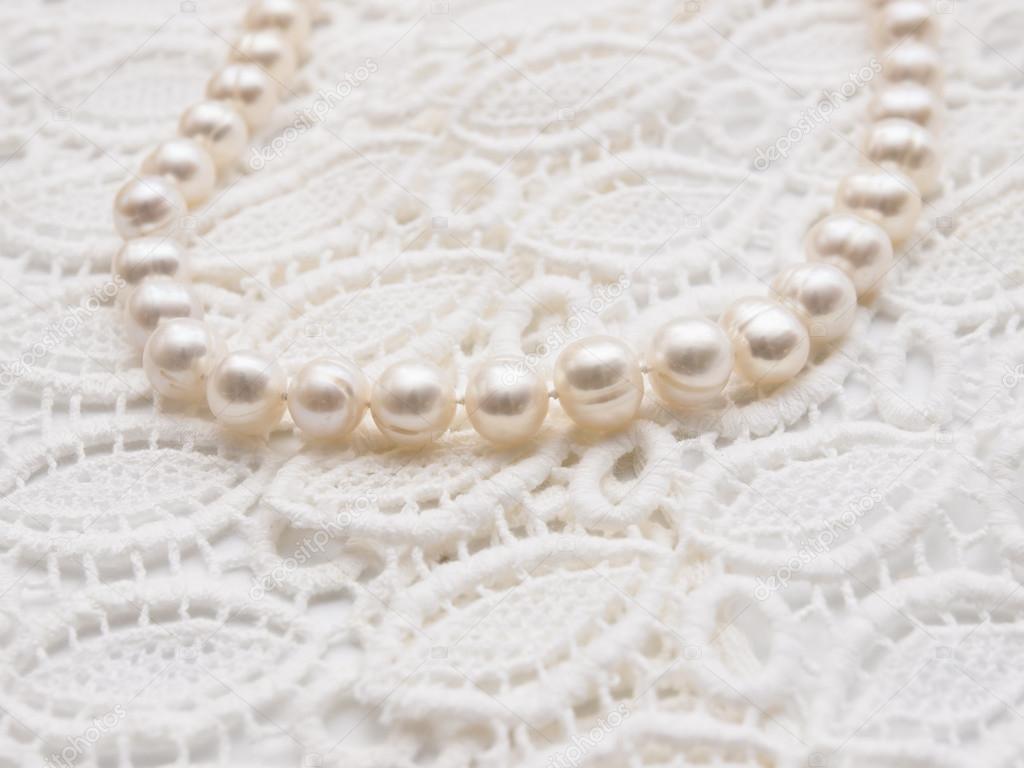 White pearl necklace on white lace background