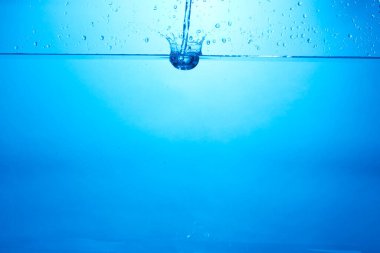 Mavi arka planda su şişesi düşüyor, damlalar düşüyor ve sıçrıyor. Su kabarcıkları dokusu